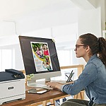 Une femme assise à un bureau, concentrée sur son travail, avec une imprimante Xerox® C320 couleur