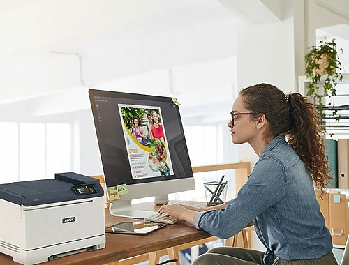 Une femme assise à un bureau, concentrée sur son travail, avec une imprimante Xerox® C320 couleur