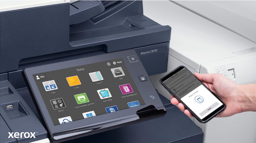 Xerox® ConnectKey® : impression et numérisation mobiles Gros plan de la main d'une personne tenant un smartphone, qui est connecté sans fil au panneau de commande à écran tactile d'une imprimante multifonction Xerox, mettant en valeur les capacités d'impression et de numérisation mobiles transparentes de Xerox ConnectKey.